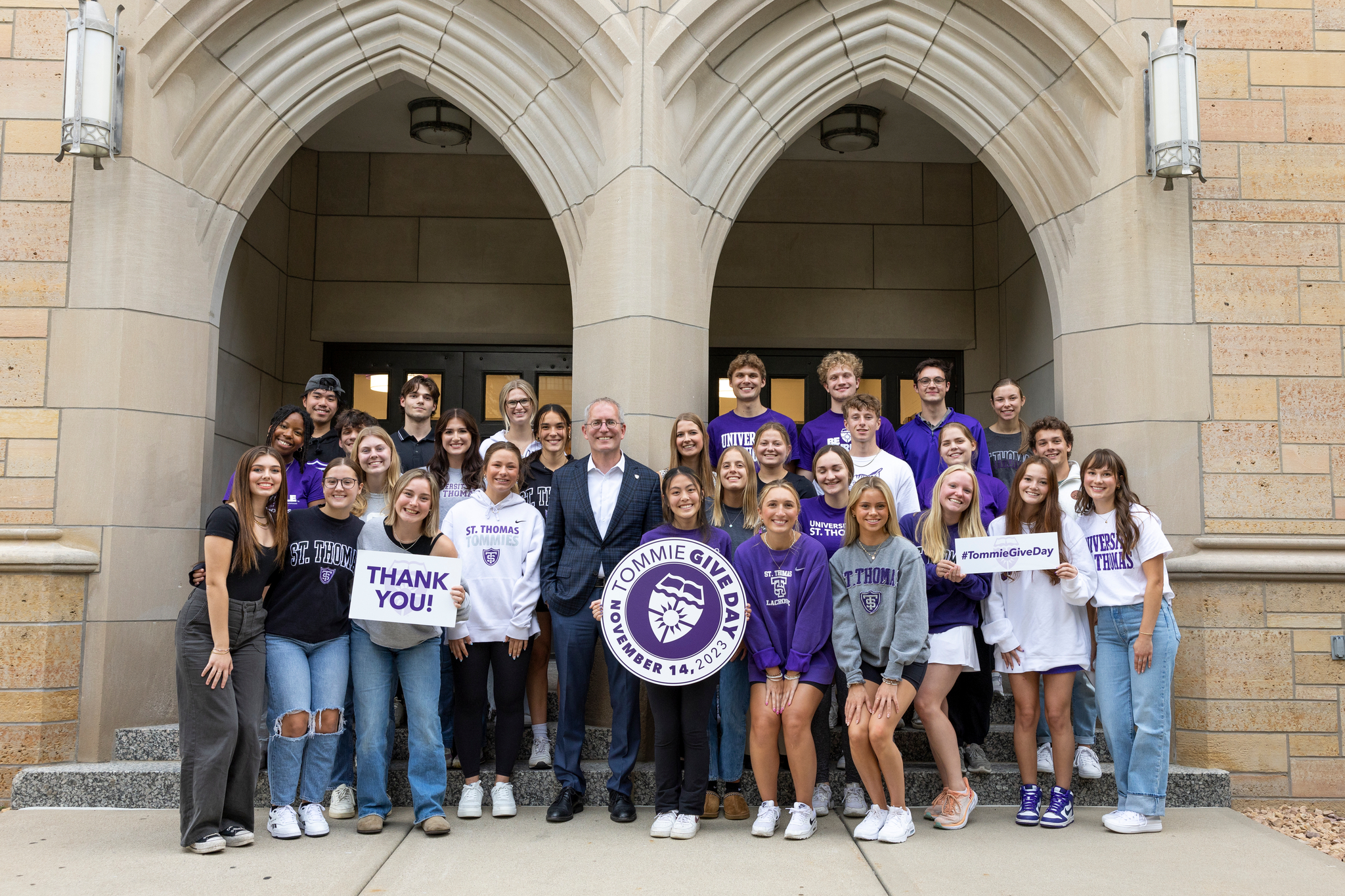 Group of 20 Tommie students in purple holding a Tommie Give Day flag