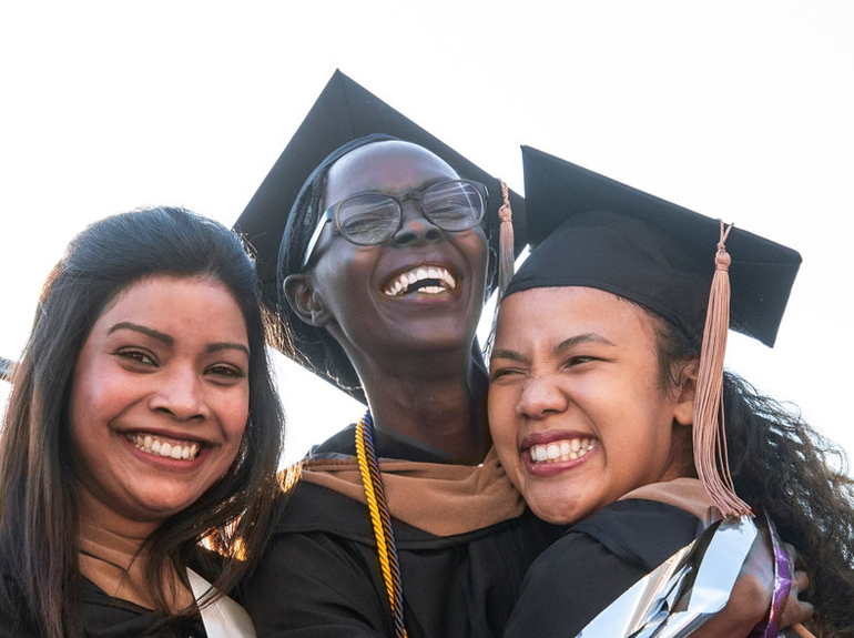 three female students embrace after a commencement ceremony