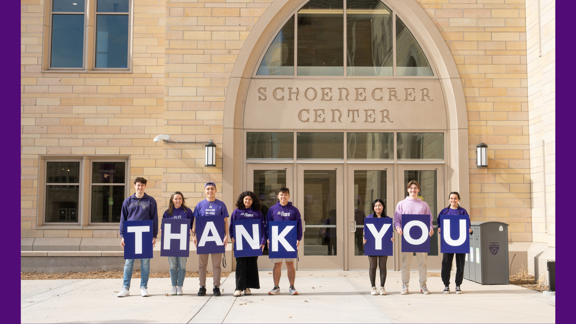 Front doors of the Schoenecker Center with students in purple holding thank you signs