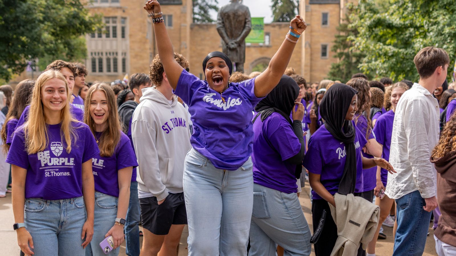 Students smile and jump for joy as they march through the arches on a sunny day on St. Paul campus.