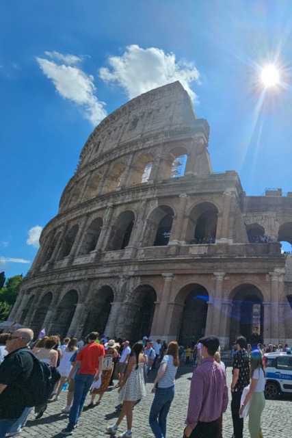 A view of the Coliseum from a crowded street outside on a sunny day during the 2024 International Tour of Italy and Austria.