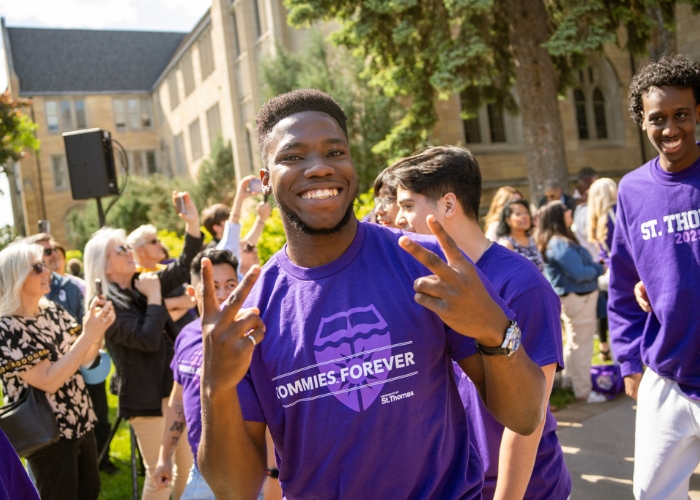 A student smiles and waves into the camera at March Out of the Arches