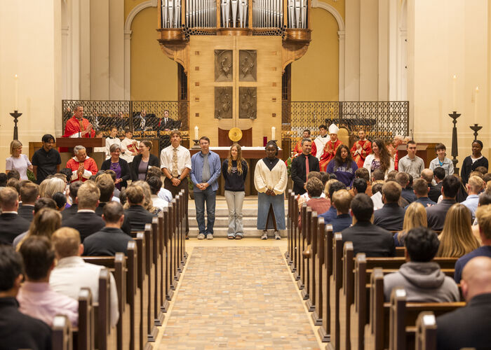 Students stand at the front of the Chapel of St. Thomas Aquinas during a campus liturgy as members of the community gather