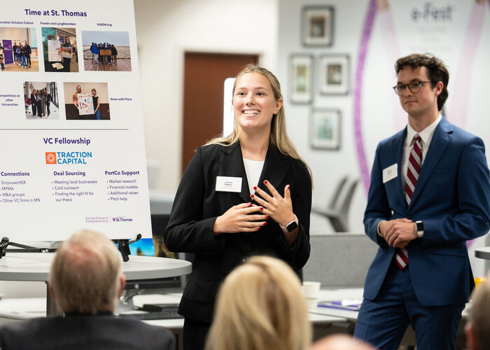 Students in business suits present a poster to a group