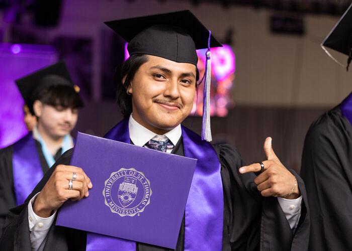 Man in a graduation cap and robe, pointing at his St. Thomas diploma case.