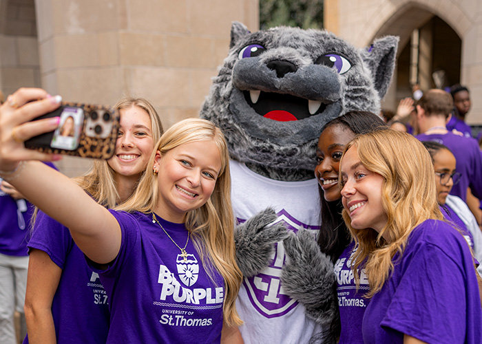 A group of 3 students take a selfie photo with the Tommie mascot