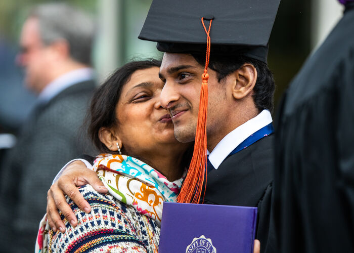 A mother kissing her son who is dressed in a graduation cap and gown.
