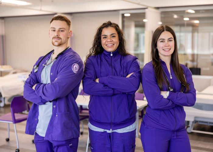 Three students pose in purple scrubs in the School of Nursing lab
