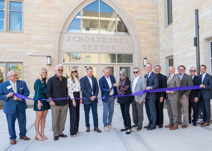 St. Thomas donors, staff and community members smile in front of the new Schoenecker Center as the Schoeneckers cut the purple ribbon to signify its opening.