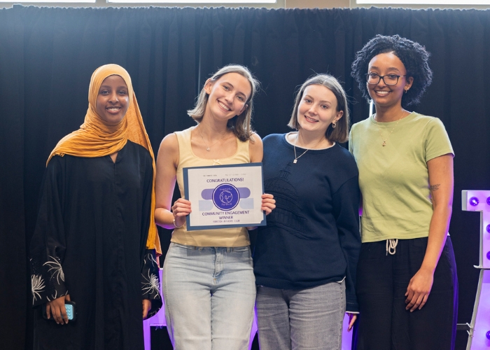 A group of four students pose with an award on a stage in Anderson Student Center