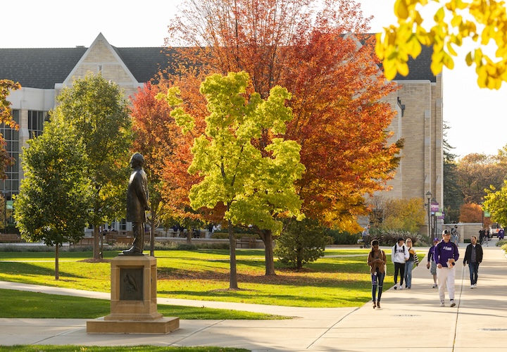 A sunny fall landscape shows Anderson Student Center and the John Ireland statue surrounded by trees in bright fall colors.