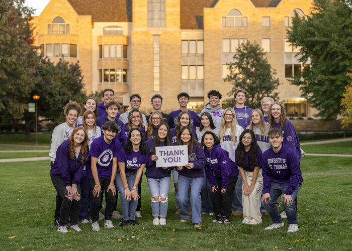 Students pose with a thank you sign during a Tommie Give Day photoshoot on campus.