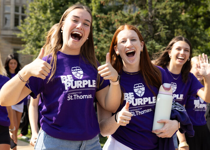 Students wearing purple St. Thomas t-shirt smile and pose during an outdoor campus event