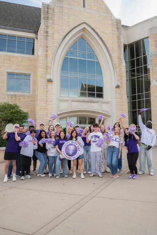 A group of students holding signs in front of the Arches while wearing purple and white