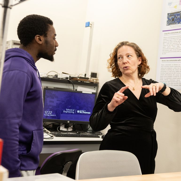 A faculty member explains the content of a poster to a student in a purple sweatshirt