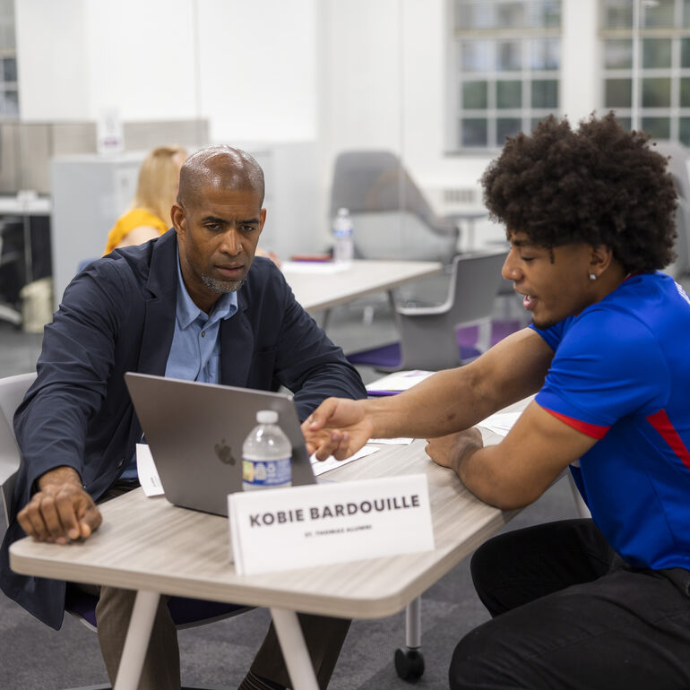 Two people sit together at a table, reviewing information on a laptop during a mentoring event.