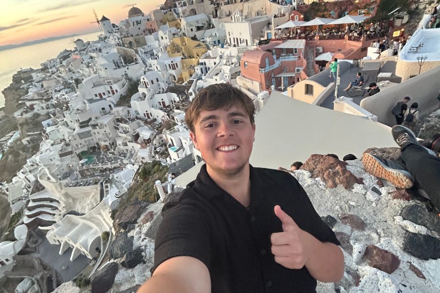 Aidan takes a selfie with a picturesque background of white buildings in Greece