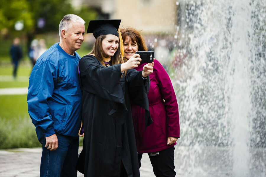 Student taking selfie with parents after graduation ceremony.