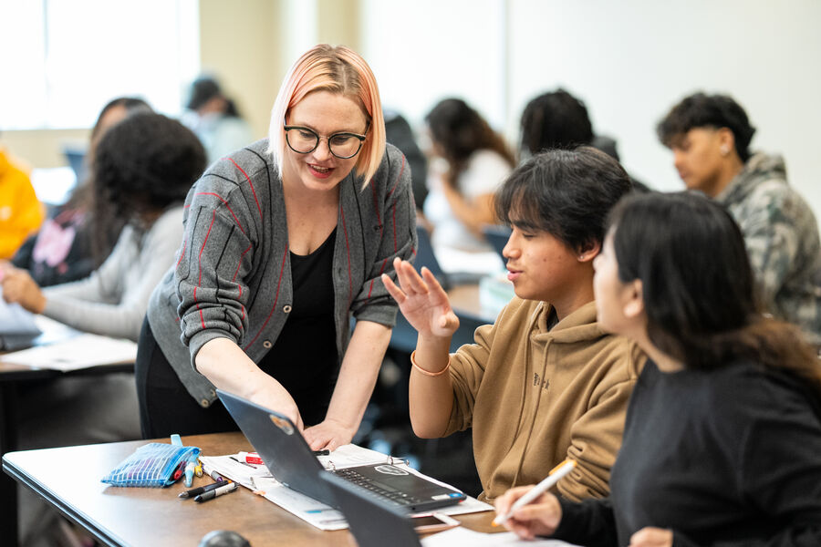In a classroom, a professor leans over and points while talking to two students