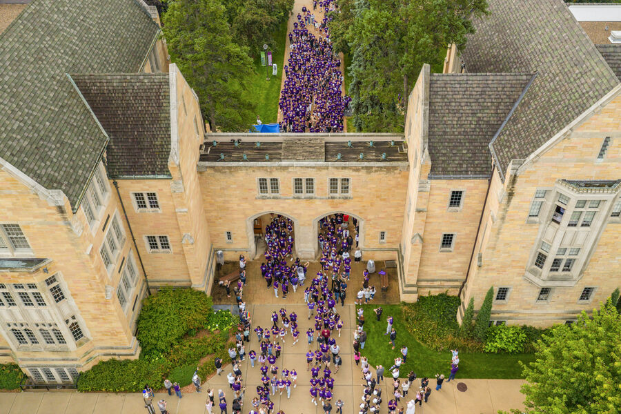 An aerial view shows a large group of students passing through the Arches as families and supporters line the walkways on campus.