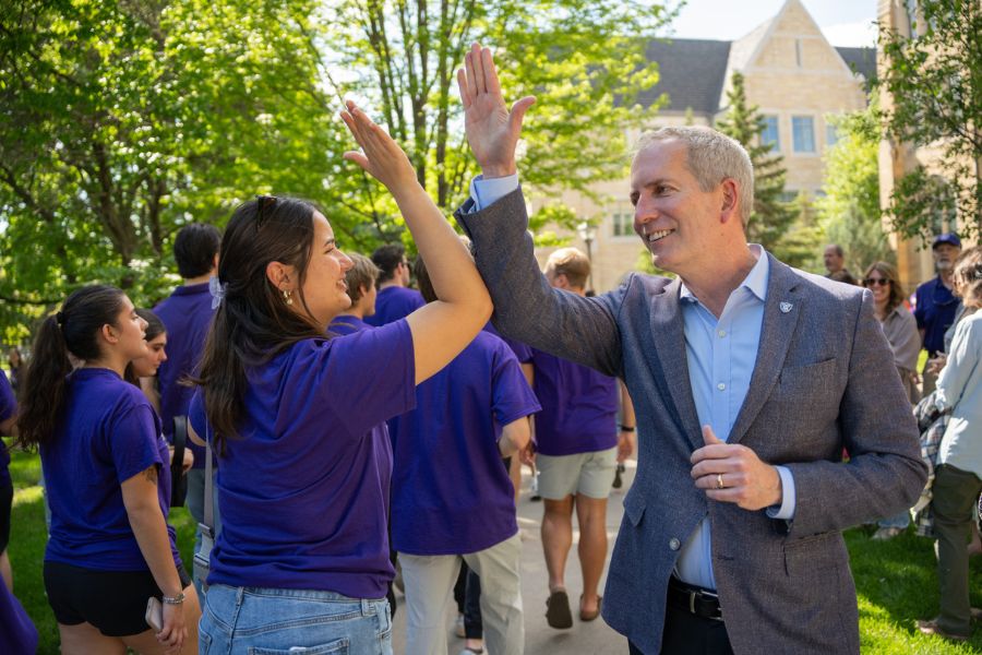 President Vischer gives a high-five to a student wearing a purple shirt at March Out of the Arches