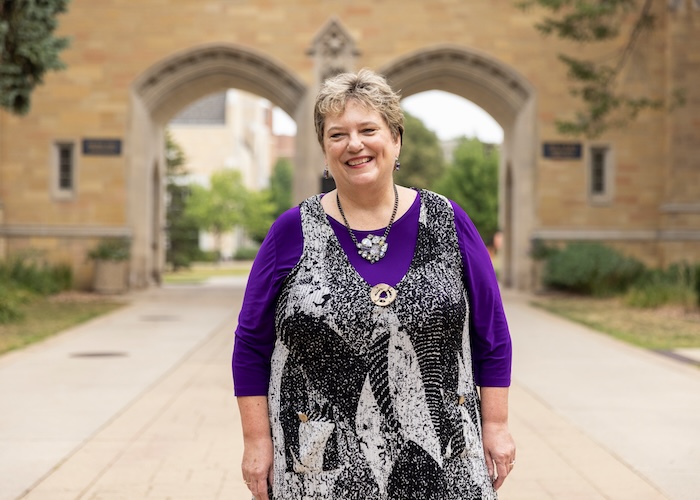 Karen Lange, vice president for Student Affairs, poses for a photo in front of The Arches, on August 5, 2021 in St. Paul. She's wearing a purple shirt with a black and white vest and smiling into the camera.