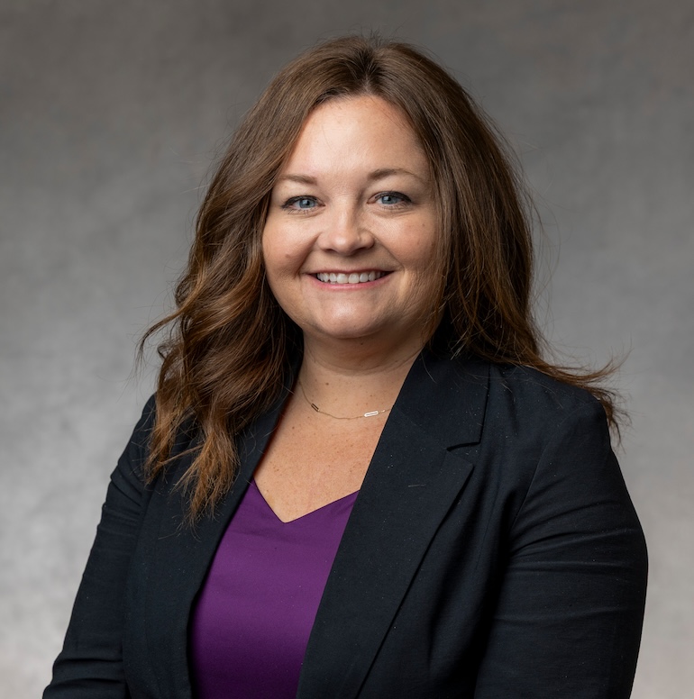 Becky Busselman smiles for a studio portrait taken against a gray background.