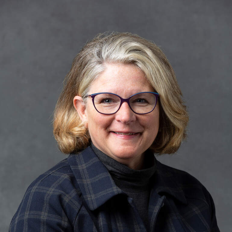 Studio headshot of Linda Baughman, Dean of Students, taken on March 22, 2023, in St. Paul. Linda smiles into the camera and wears a blue flannel shirt.