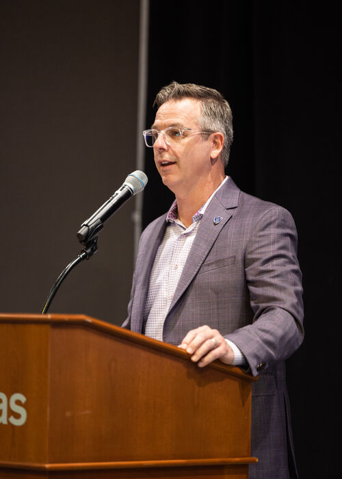 A man with clear-frame glasses speaks from podium